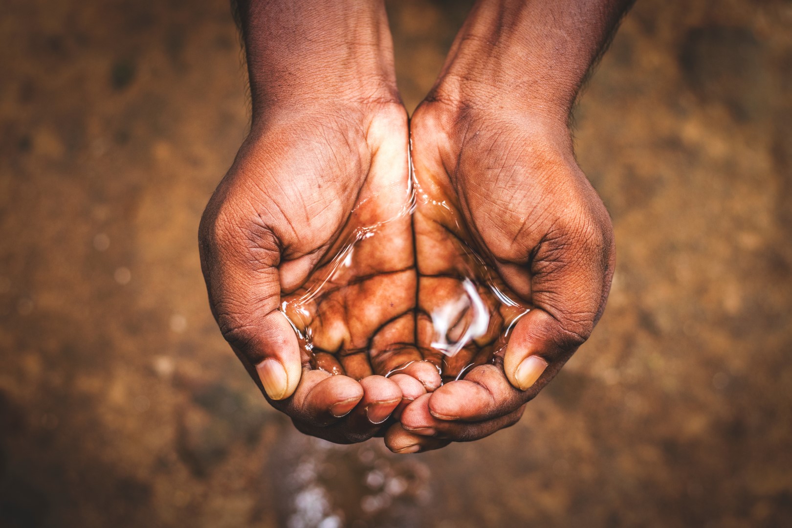 Two hands holding clean water – symbol of a Kenyan aid project providing sustainable drinking water, reducing CO₂ emissions, improving health, and supporting education.