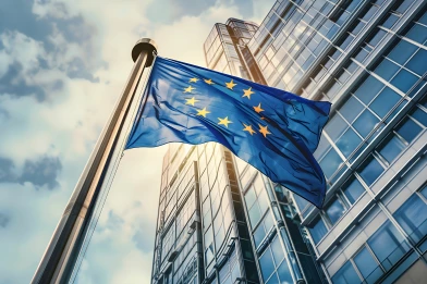 European Union flag in front of a modern office building, symbolizing the new EBA regulations and sanctions screening requirements starting in 2025