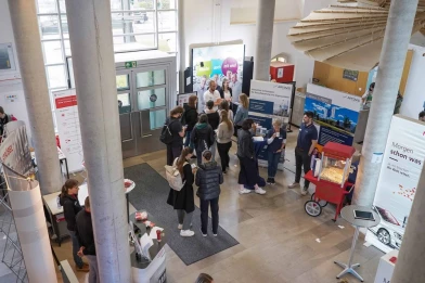 The image shows the Companies@Campus Ansbach event with students engaging in discussions at various company booths. It represents university career fairs where employers connect directly with students and graduates. In this context, ISO-Gruppe positions itself as an attractive IT employer offering diverse career opportunities and long-term development paths.