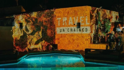Das Bild zeigt das Travel Unchained Event von Chain4Travel 2025, bei dem die ISO-Gruppe als Partner vertreten ist. Vor einer illuminierten Steinwand mit der Aufschrift „Travel Unchained“ spiegelt sich die moderne Eventatmosphäre im Pool. Die Veranstaltung steht für Innovation, Networking und die Zukunft der digitalen Reisetechnologie.