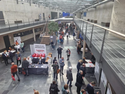 Das Bild zeigt den Empfangs- und Networkingbereich eines Fundraising-Kongresses mit Anmeldecounter, Infoständen und vielen Teilnehmenden im Austausch. Es steht für den 16. Fundraisingtag in München am 11. März 2027, bei dem Vereine und Stiftungen Impulse zu Spenden, Unternehmenskooperationen und Stiftungen erhalten. Die ISO-Gruppe ist mit Charity:up vor Ort und zeigt, wie personalisierte Videos Spenden oder Newsletter-Abos direkt im Video ermöglichen – ohne Medienbrüche.