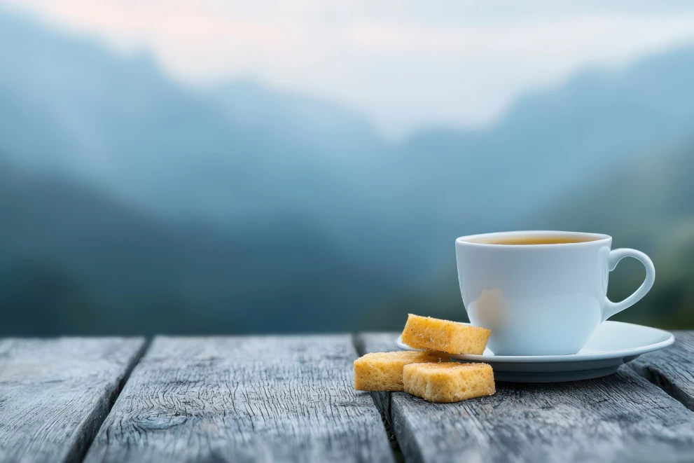 Cup of tea and pastries on a wooden table with a mountain view in the background – symbolic representation of catering during training breaks at ISO-Gruppe.