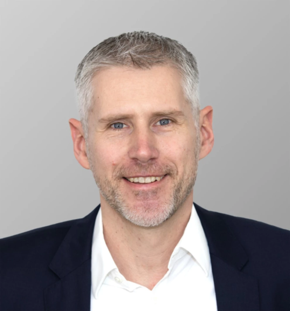 Porträtfoto von Claus Bogner, Board-Mitglied der ISO-Gruppe, verantwortlich für Produktion und Entwicklung. Er trägt ein weißes Hemd, einen dunkelblauen Anzug und hat kurze graue Haare.