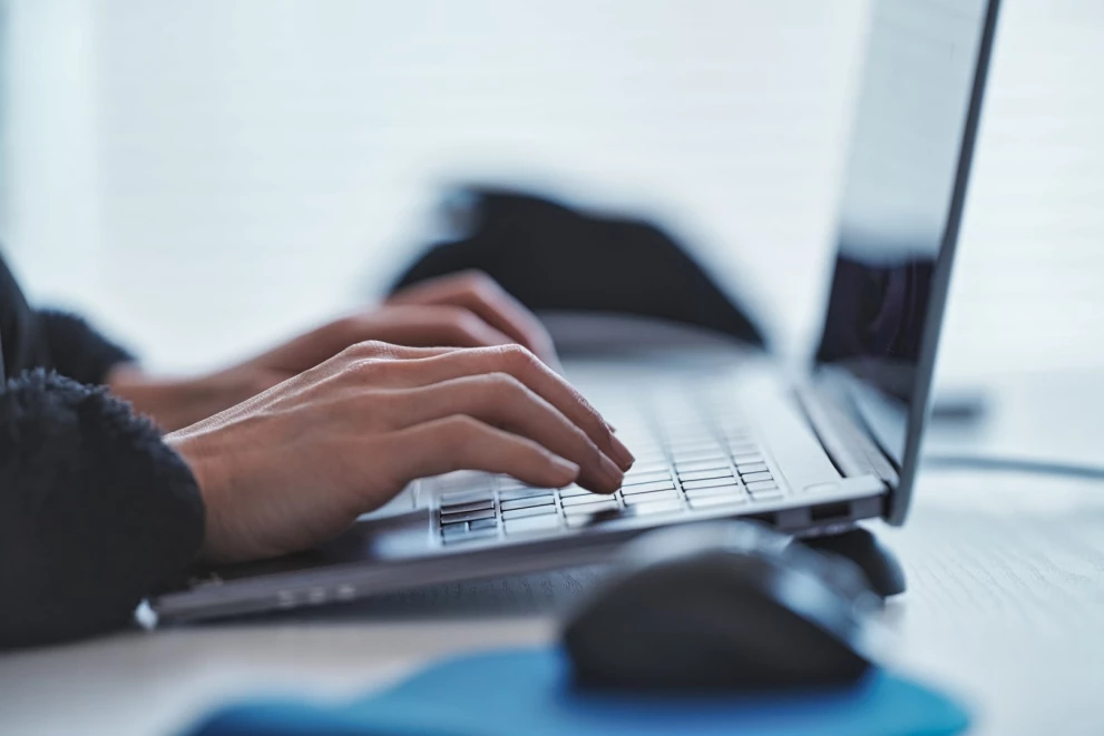 Hände tippen auf einem Laptop, daneben eine Computermaus – typische Arbeitsumgebung während einer Schulung bei der ISO-Gruppe.