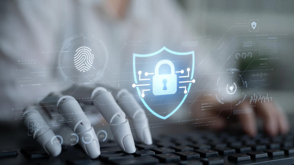 A robotic and human hand at a keyboard with a security lock overlay represents an autonomous security operations center. It fits topics like AI in cybersecurity, automated alert triage, SOAR playbooks, and faster incident response for enterprise environments.