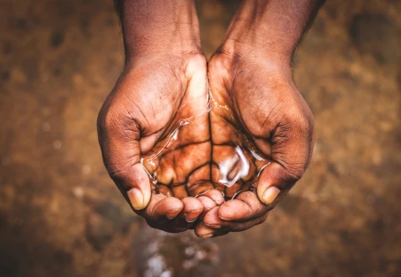 Zwei Hände halten sauberes Wasser – Symbol für ein Hilfsprojekt in Kenia, das durch nachhaltige Trinkwasserversorgung CO₂-Emissionen reduziert, Gesundheit schützt und Bildung fördert.